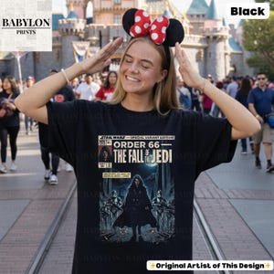 May include: Black t-shirt featuring a comic book-style graphic from Star Wars: Order 66 - The Fall of the Jedi. The design includes text and illustrations of characters and scenes from the Star Wars universe. The shirt is a special edition.