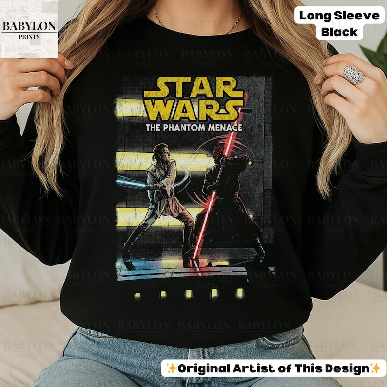 Puede incluir: Camiseta negra de manga larga con un gr&aacute;fico de Star Wars. El dise&ntilde;o incluye el texto "STAR WARS THE PHANTOM MENACE" y una ilustraci&oacute;n de dos personajes con sables de luz. La camiseta tambi&eacute;n tiene el texto "Long Sleeve Black".