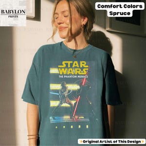 Puede incluir: Camiseta color abeto con un gr&aacute;fico de Star Wars: La Amenaza Fantasma. El dise&ntilde;o incluye el logotipo de Star Wars y personajes con sables de luz. La camiseta es de Babylon Prints y est&aacute; etiquetada como Comfort Colors.