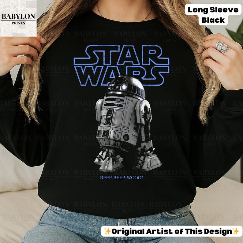 K&ouml;nnte beinhalten: Schwarzes Langarmshirt mit dem Star Wars-Logo in Blau und einer detaillierten Grafik von R2-D2. Der Text "BEEP-BEEP-WOOO!" befindet sich unter dem Droiden. Das Shirt hat auch den Text "Long Sleeve Black".