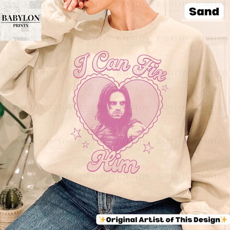 May include: Sand-colored sweatshirt with the text "I Can Fix Him" in pink script, surrounding a pink heart-shaped graphic with a portrait. The design includes stars and the words "Original Artist of This Design."