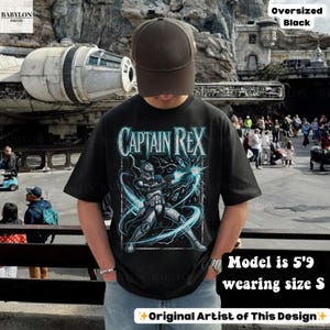 May include: Black oversized t-shirt with a Captain Rex graphic and blue lightning. The text "CAPTAIN REX" is in a stylized font. The model is 5'9" and wearing size S. The design is by the original artist.