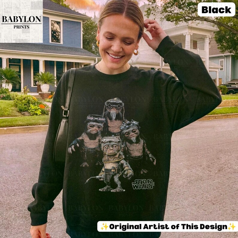 Op de afbeelding: Een zwart sweatshirt met lange mouwen en een grafische print van vier Ewok-personages uit Star Wars. Het ontwerp bevat het Star Wars-logo in witte tekst. Het sweatshirt heeft een ronde hals en geribbelde boorden.