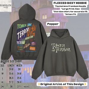 Op de afbeelding: Pepperkleurige fleece boxy hoodie met de tekst "TOWER OF TERROR" op de voorkant en een afbeelding op de achterkant. De afbeelding op de achterkant bevat de tekst "Twice the Fright" en "Hollywood Tower". De maattabel van de hoodie is inbegrepen.