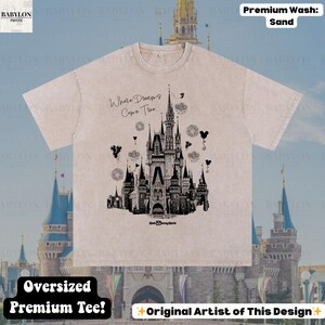 May include: Sand-coloured oversized premium tee featuring a black graphic of a castle with the text "Where Dreams Come True." The design includes Mickey Mouse balloons and fireworks. The shirt is from the original artist.