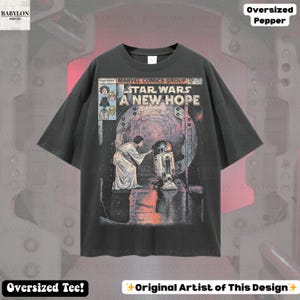 May include: Dark gray oversized t-shirt featuring a Star Wars comic book cover. The graphic includes the text "STAR WARS A NEW HOPE" and images of Princess Leia and R2-D2. The shirt also has the text "Oversized Tee!" and "Original Artist of This Design".