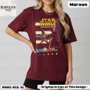 Puede incluir: Camiseta burdeos de Star Wars con un gr&aacute;fico de "La Amenaza Fantasma". El dise&ntilde;o incluye personajes con sables de luz y el logo de Star Wars en amarillo. Talla XL.