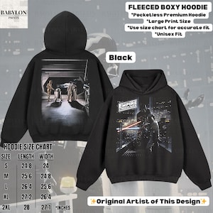 May include: Black fleeced boxy hoodie with a Star Wars design. The front features a scene from "Empire Strikes Back", and the back shows a scene with C-3PO, R2-D2, and Yoda. The hoodie has a large print size and is available in sizes S (24.8" length, 24" width) to 2XL (28" length, 27.1" width).