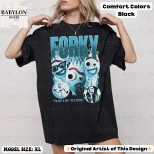 May include: Black t-shirt featuring the word "FORKY" in teal, with cartoon fork characters. The shirt includes the text "I'M NOT A TOY. I'M A SPORK!" and is labeled "Comfort Colors Black" and "MODEL SIZE: XL".