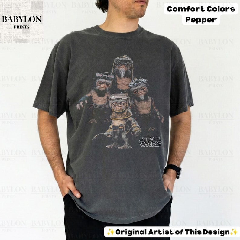 Op de afbeelding: Een antracietgrijs t-shirt met korte mouwen en een grafische print van vier Ewok-personages uit Star Wars. Het shirt is gelabeld als Comfort Colors Pepper en bevat het Star Wars-logo in het wit rechtsonder op de afbeelding.