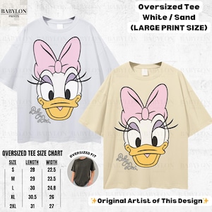 May include: Two oversized t-shirts, one white and one sand-colored, each featuring a large print of Daisy Duck's face with a pink bow. The shirts have the text "Baby Duck" below the graphic. The image also includes a size chart.