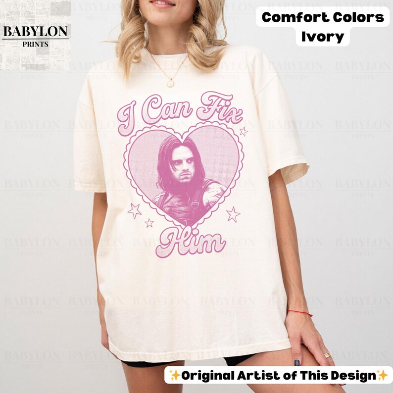 May include: Ivory-colored t-shirt with the text "I Can Fix Him" in pink, featuring a heart-shaped graphic with a portrait. The shirt is from Comfort Colors and has the Babylon Prints logo.
