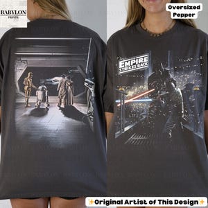 May include: Dark gray oversized t-shirt featuring scenes from "The Empire Strikes Back." The front graphic shows Darth Vader in a lightsaber battle, while the back displays C-3PO, R2-D2, and other characters. The shirt has the text "The Empire Strikes Back."