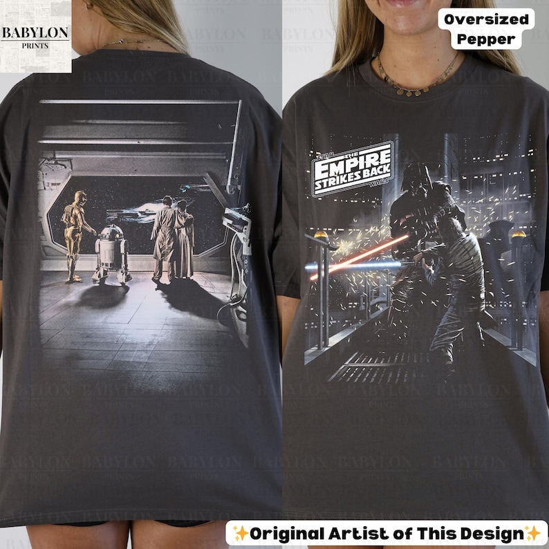 May include: Dark gray oversized t-shirt featuring scenes from "The Empire Strikes Back." The front graphic shows Darth Vader in a lightsaber battle, while the back displays C-3PO, R2-D2, and other characters. The shirt has the text "The Empire Strikes Back."