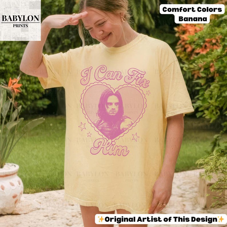May include: A light yellow t-shirt with the text "I Can Fix Him" in pink, featuring a heart-shaped graphic with a portrait. The shirt also has the text "Comfort Colors Banana" and "Original Artist of This Design".