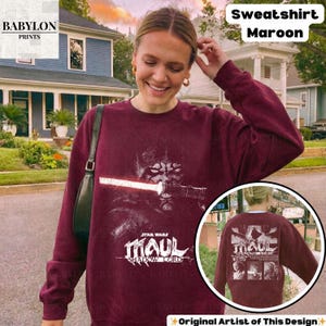 May include: Maroon sweatshirt featuring a Star Wars graphic of Darth Maul with a lightsaber. The text "STAR WARS MAUL SHADOW LORD" is below the graphic. The sweatshirt also has the text "Sweatshirt Maroon" on the top right.