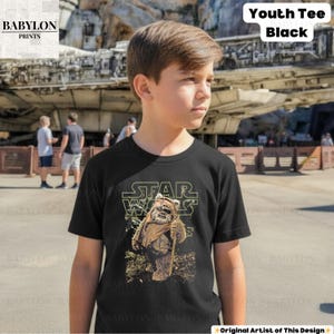 May include: Black youth tee featuring a Star Wars design with the text "STAR WARS" above an Ewok character holding a staff. The shirt also has the text "Youth Tee Black". The Babylon Prints logo is in the upper left corner.