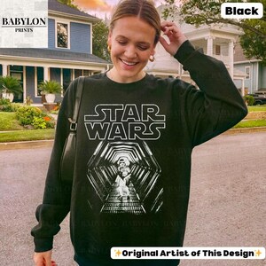 May include: Black Star Wars sweatshirt with a white graphic of the Star Wars logo and a tunnel design. The sweatshirt has long sleeves and a crew neck. The text "BABYLON PRINTS" is in the upper left corner, and "Original Artist of This Design" is at the bottom.