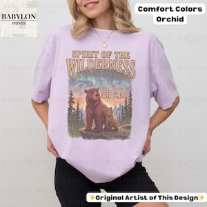May include: Orchid-coloured t-shirt with a graphic featuring two bears and the text "Spirit of the Wilderness." The design includes the words "Brother Bear" and "Northern Adventure." The shirt is from Babylon Prints.