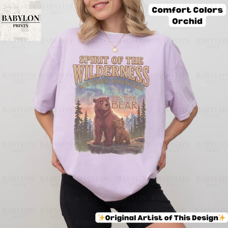 May include: Orchid-coloured t-shirt with a graphic featuring two bears and the text "Spirit of the Wilderness." The design includes the words "Brother Bear" and "Northern Adventure." The shirt is from Babylon Prints.
