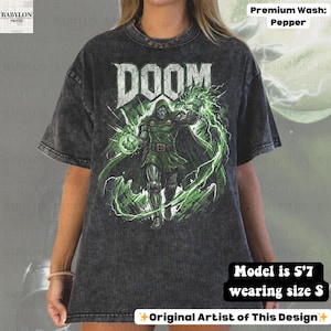 May include: A dark gray t-shirt with a graphic of a character from the word "DOOM". The character is wearing green armor and cape, with green energy effects. The shirt has the text "DOOM" in white.