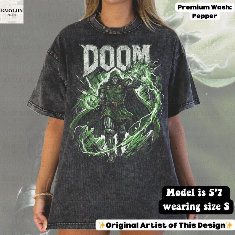 May include: A dark gray t-shirt with a graphic of a character from the word "DOOM". The character is wearing green armor and cape, with green energy effects. The shirt has the text "DOOM" in white.