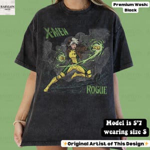 May include: Black t-shirt with a graphic of Rogue from X-Men. The design includes the text "X-MEN" and "ROGUE" in green. The character is in a yellow and green costume, with green energy effects. The shirt is a premium wash.
