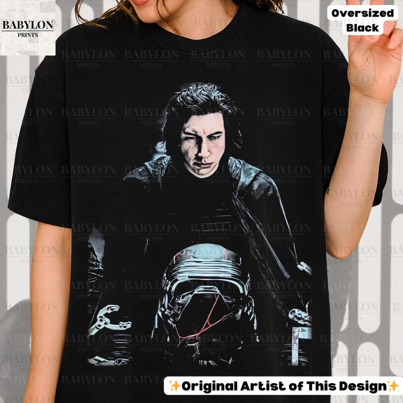 May include: Black oversized t-shirt with a portrait of a character with long hair and a helmet. The text "Original Artist of This Design" is at the bottom. The shirt is a dark colour.