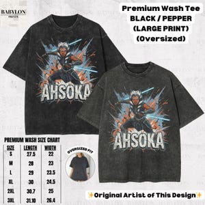 Może przedstawiać: Dwie czarne koszulki w rozmiarze oversize z dużym nadrukiem graficznym Ahsoki Tano z Gwiezdnych Wojen. Poniżej znajduje się napis "AHSOKA". Obraz zawiera r&oacute;wnież tabelę rozmiar&oacute;w.