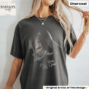 K&ouml;nnte beinhalten: Anthrazitfarbenes T-Shirt mit einer detaillierten Grafik von Darth Vader. Das Design enth&auml;lt den Text "Darth Vader" in einer stilisierten Schrift. Das Shirt hat eine lockere Passform und stammt von Babylon Prints.