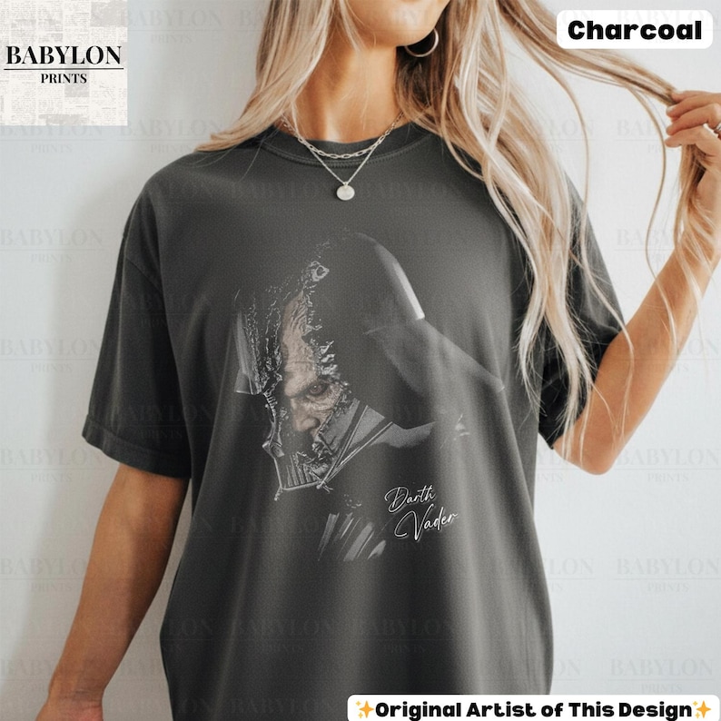 K&ouml;nnte beinhalten: Anthrazitfarbenes T-Shirt mit einer detaillierten Grafik von Darth Vader. Das Design enth&auml;lt den Text "Darth Vader" in einer stilisierten Schrift. Das Shirt hat eine lockere Passform und stammt von Babylon Prints.