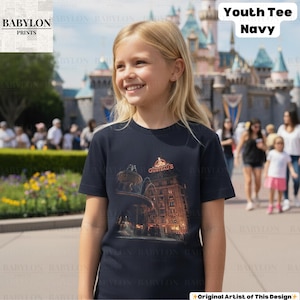 May include: Navy blue youth tee with a graphic of a building and the text "GUSTEAU'S". The tee is a crew neck style. The words "Youth Tee Navy" are printed in white. The shirt is worn by a young person. The image is taken outdoors.
