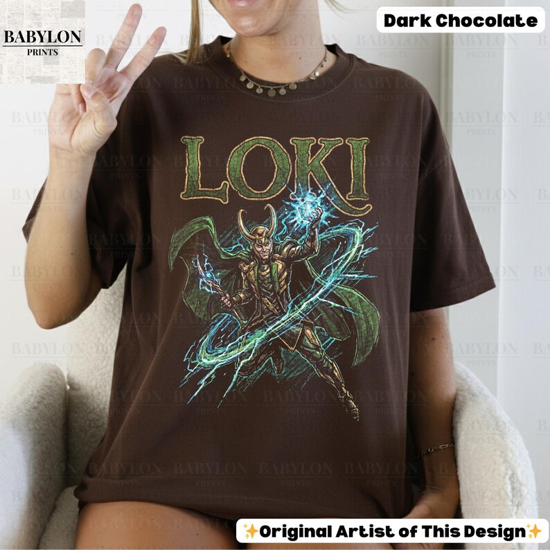 May include: Dark chocolate-colored t-shirt featuring the word "LOKI" in green, above a detailed illustration of a character with green cape and horns, wielding blue energy. The shirt is from Babylon Prints.