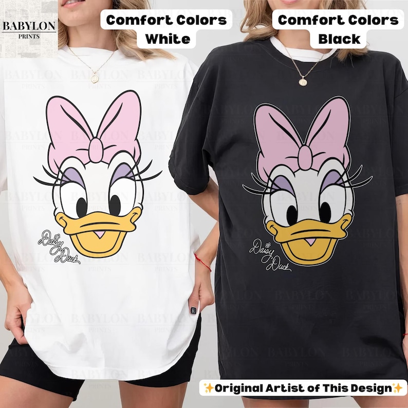 May include: White and black t-shirts featuring a Daisy Duck graphic. The design includes a pink bow, eyelashes, and the text "Daisy Duck". The shirts are labeled "Comfort Colors" and "Original Artist of This Design".