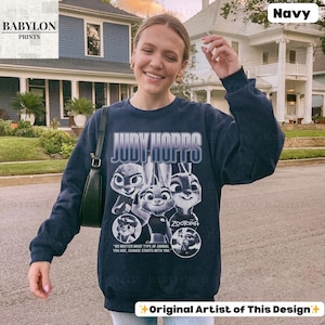 May include: Navy blue sweatshirt featuring the text "JUDY HOPPS" and images of characters from the movie Zootopia. The sweatshirt also includes the text "NO MATTER WHAT TYPE OF ANIMAL YOU ARE, CHANGE STARTS WITH YOU." and "ZOOTOPIA."