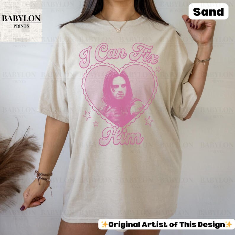 May include: Sand-colored t-shirt with the text "I Can Fix Him" in pink script, surrounding a pink heart-shaped graphic with a portrait. The shirt has short sleeves and a relaxed fit.