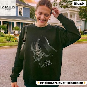 K&ouml;nnte beinhalten: Schwarzes Sweatshirt mit Darth Vader-Grafik. Das Design zeigt eine detaillierte Illustration von Darth Vaders Helm und Gesicht mit dem Text "Darth Vader". Das Sweatshirt stammt von "Babylon Prints".