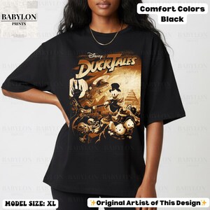 May include: Black t-shirt featuring a graphic from Disney's DuckTales. The design is in shades of brown and gold, with the show's title prominently displayed. The shirt also has the text "Comfort Colors Black" and "Original Artist of This Design".