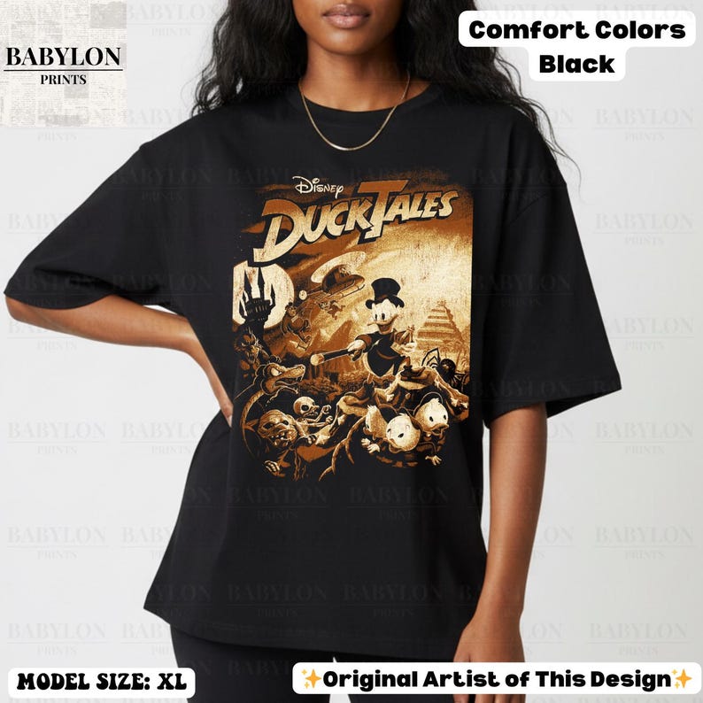 May include: Black t-shirt featuring a graphic from Disney's DuckTales. The design is in shades of brown and gold, with the show's title prominently displayed. The shirt also has the text "Comfort Colors Black" and "Original Artist of This Design".