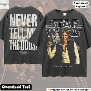 Puede incluir: Camiseta gris oscuro de gran tama&ntilde;o con tem&aacute;tica de Star Wars. La parte delantera muestra a Han Solo con el logo de Star Wars, y la trasera tiene el texto "NEVER TELL ME THE ODDS". La camiseta tiene un corte holgado, adecuada para uso casual.