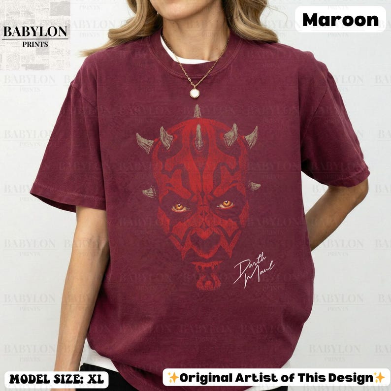 Może przedstawiać: Bordowa koszulka z czerwoną grafiką twarzy Darth Maula, z rogami i ż&oacute;łtymi oczami. Tekst "Darth Maul" jest napisany białą czcionką. Koszulka ma tekst "BABYLON PRINTS" w lewym g&oacute;rnym rogu.