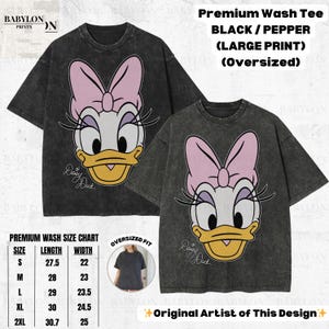 May include: Two black oversized t-shirts with a large Daisy Duck graphic. The graphic features Daisy's face with a pink bow, white face, and yellow beak. The shirts have a premium wash and are available in sizes S to 2XL.