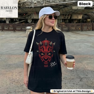 Może przedstawiać: Czarny t-shirt z czerwoną grafiką twarzy Darth Maula, z rogami i ż&oacute;łtymi oczami. Tekst "Darth Maul" jest biały. Koszulka jest od Babylon Prints.