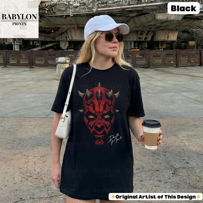 Może przedstawiać: Czarny t-shirt z czerwoną grafiką twarzy Darth Maula, z rogami i ż&oacute;łtymi oczami. Tekst "Darth Maul" jest biały. Koszulka jest od Babylon Prints.