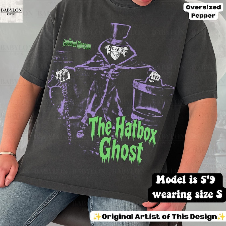 Puede incluir: Una camiseta gris carb&oacute;n de manga corta con un gr&aacute;fico de The Hatbox Ghost de The Haunted Mansion. El dise&ntilde;o muestra al personaje con sombrero de copa, sosteniendo un bast&oacute;n y una sombrerera, con el texto The Haunted Mansion y The Hatbox Ghost.
