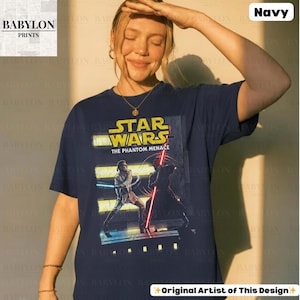Puede incluir: Camiseta azul marino con un dise&ntilde;o de Star Wars: La Amenaza Fantasma. El dise&ntilde;o incluye el logotipo de Star Wars y personajes con sables de luz. Tambi&eacute;n se ve el texto "Original Artist of This Design".