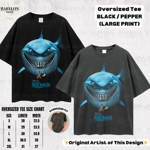 May include: Two oversized black and pepper-colored t-shirts with a large print of a shark from the movie "Finding Nemo." The shark is blue with a wide grin. The shirts have a size chart and the text "Original Artist of This Design."