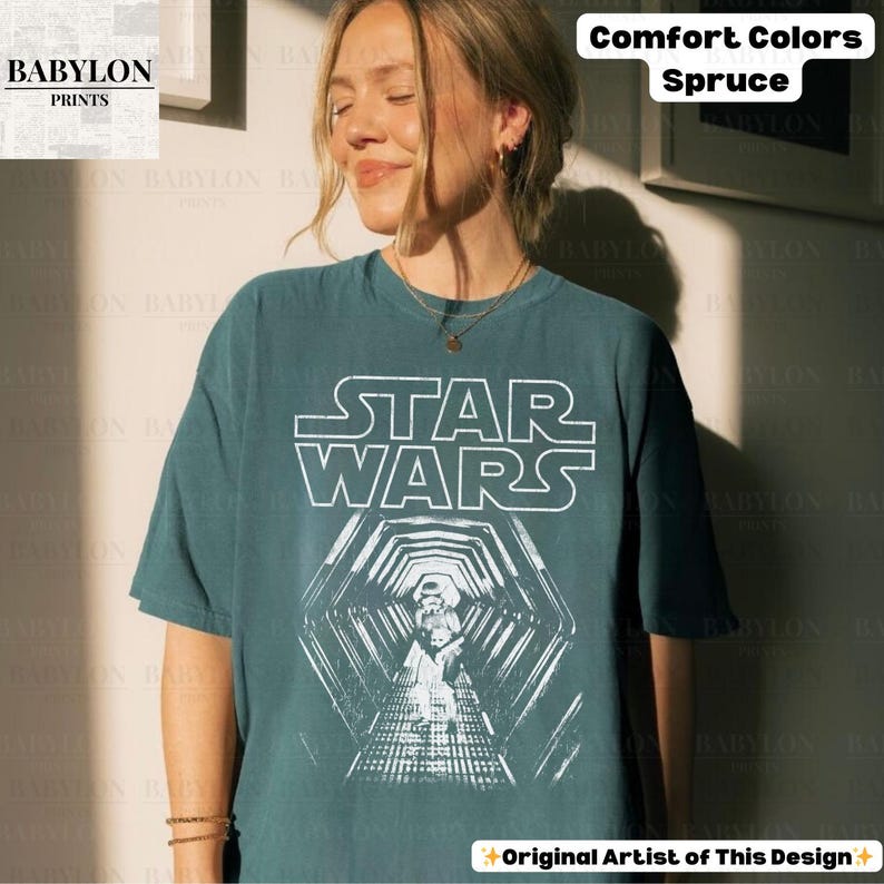May include: A spruce-colored Star Wars graphic t-shirt. The white graphic features the Star Wars logo and a tunnel scene with a Stormtrooper. The shirt is a comfort color and has a relaxed fit. The Babylon Prints logo is in the upper left corner.