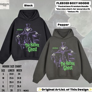 Puede incluir: Dos sudaderas con capucha boxy de felpa en colores negro y pimienta, con un gr&aacute;fico de The Hatbox Ghost en morado y verde. El texto dice Haunted Mansion y The Hatbox Ghost. Se incluye una tabla de tallas con medidas en pulgadas de la S a la 2XL.