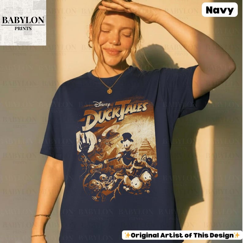 May include: Navy blue t-shirt featuring a vintage-style graphic from Disney's DuckTales. The design includes various characters and the show's logo in a distressed, aged aesthetic. The shirt is a classic crew neck.